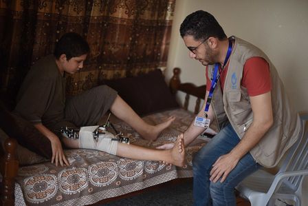 Ahmed zuhause auf seinem Bett mit einem Mitarbeiter des HI-Teams.