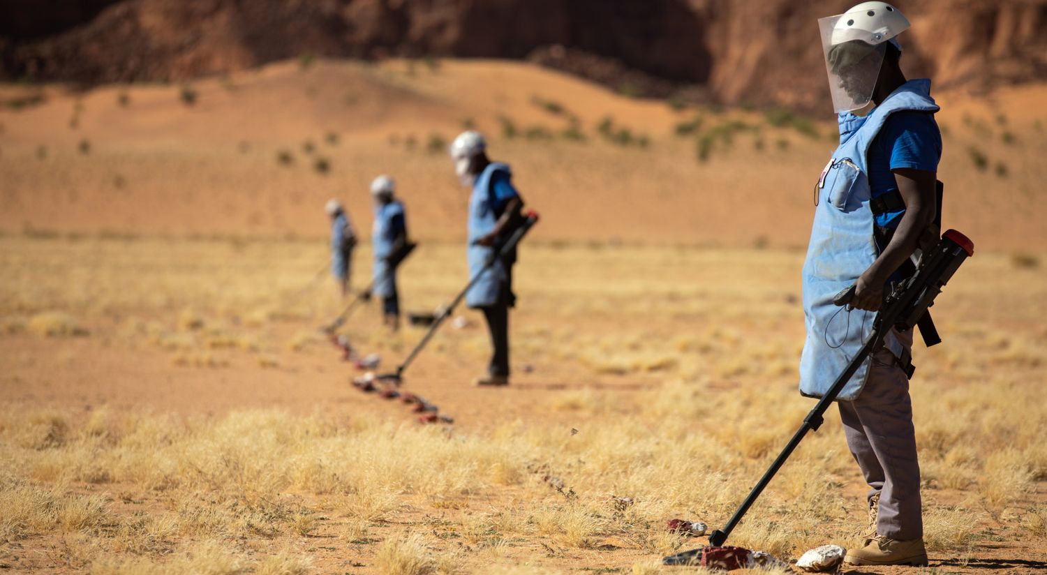 Mehrere Entminer aus dem Tschad stehen mit Ausrüstung und Detektor in einer Reihe am Rand eines Minenfeldes.