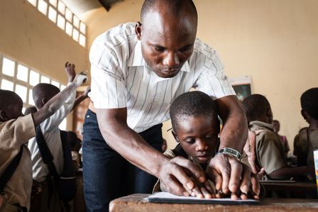 Trésor aus Togo hat eine Sehschwäche und lernt mit seinem Lehrer die Braille-Schrift.