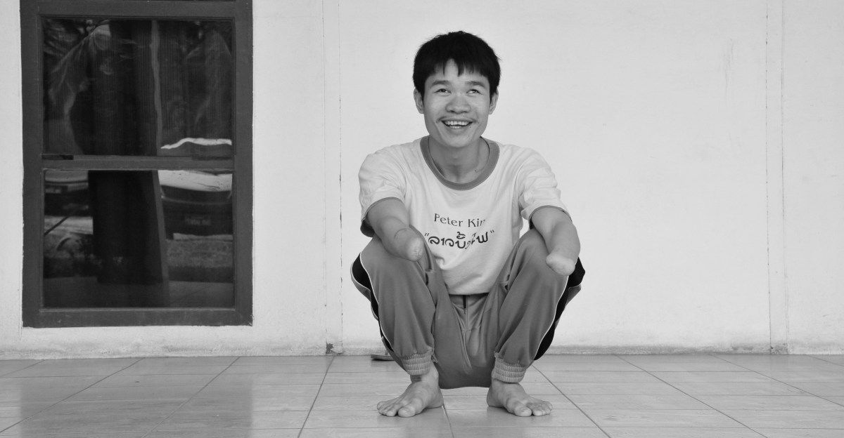 Phongsavath aus Laos hockend. Durch eine Streubombe verlor er Augenlicht und Arme.